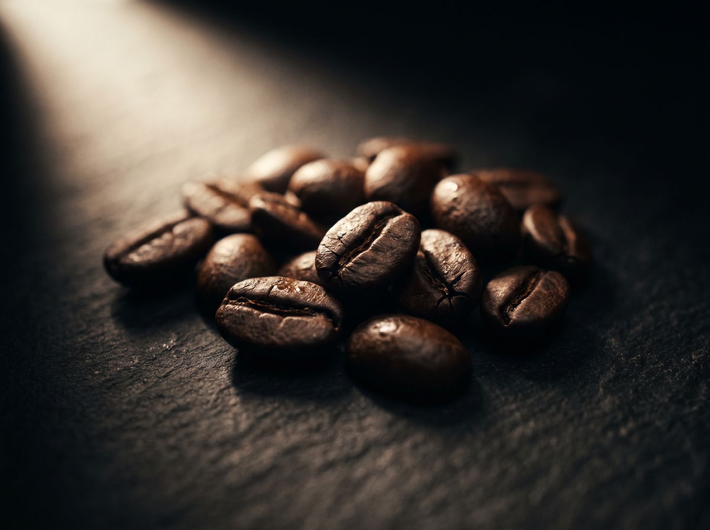 Roasted coffee beans on dark slate under a narrow shaft of warm light