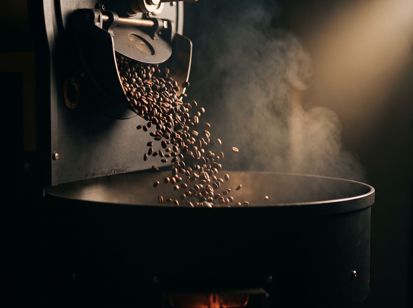 Freshly roasted beans cascading from the roaster into the cooling drum through drifting smoke